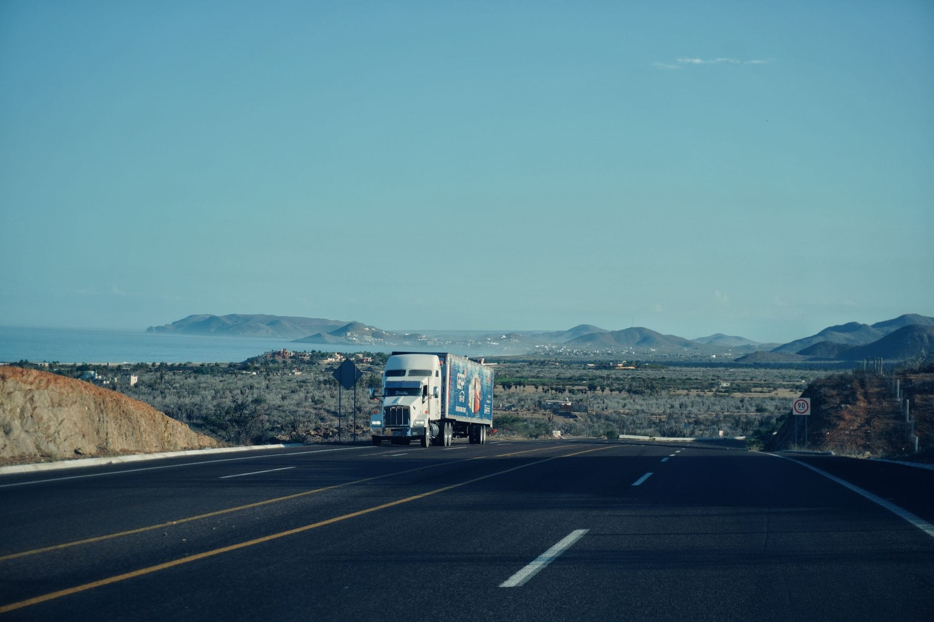 White semi-truck driving on a highway through open landscape